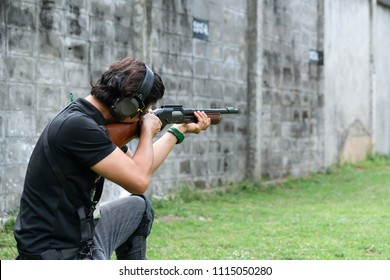 Middle Age Man Wear Ear Plug Sitting And Aiming Shotgun At Target In Shooting Range. Men Practicing Fire Pistol Shooting.