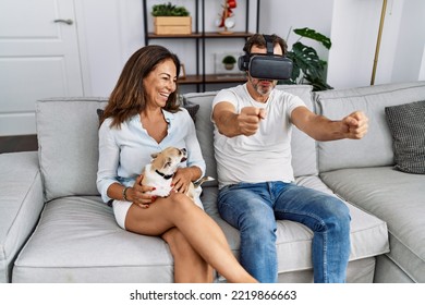 Middle Age Man And Woman Couple Using Vr Goggles Sitting On Sofa With Dog At Home