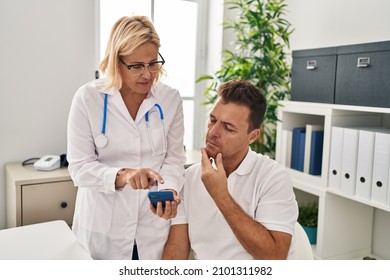 Middle Age Man And Woman Doctor And Patient Using Smartphone At Clinic