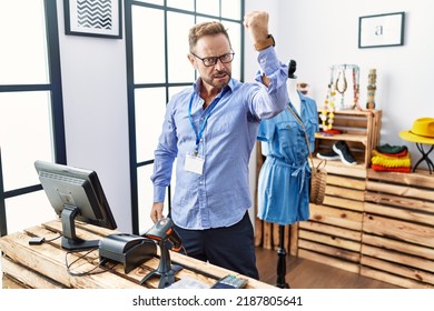 Middle age man working as manager at retail boutique angry and mad raising fist frustrated and furious while shouting with anger. rage and aggressive concept. 