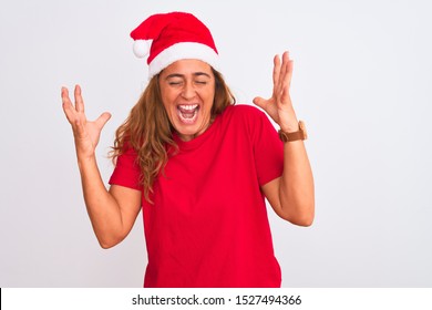 Middle age mature woman wearing christmas hat over isolated background celebrating mad and crazy for success with arms raised and closed eyes screaming excited. Winner concept - Shutterstock ID 1527494366