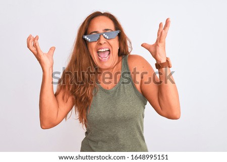 Middle age mature woman wearing thug life sunglasses over isolated background celebrating mad and crazy for success with arms raised and closed eyes screaming excited. Winner concept