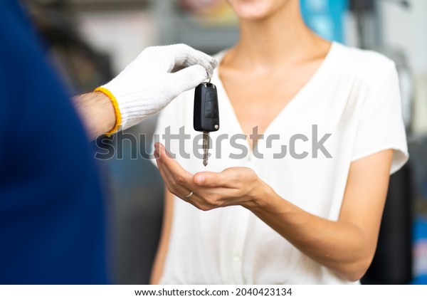 Middle age mechanic man with beard gives the car\
key to female customer at Car maintenance station and automobile\
service garage
