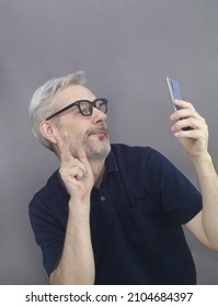 Middle Age Men With Funny Face Holding Smartphone And Looking At Phone Screen Om Gray Background