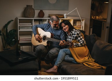 Middle Age Romantic Couple Enjoying Time Together At Home. Man Playing Acoustic Guitar. They Drinking Wine