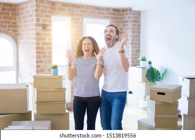 Middle age senior couple moving to a new home with boxes around celebrating mad and crazy for success with arms raised and closed eyes screaming excited. Winner concept