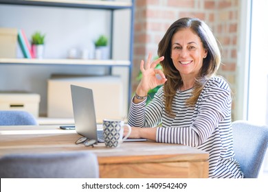 Middle age senior woman sitting at the table at home working using computer laptop doing ok sign with fingers, excellent symbol - Shutterstock ID 1409542409