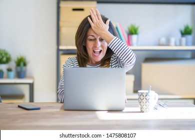 Middle Age Senior Woman Sitting At The Table At Home Working Using Computer Laptop Surprised With Hand On Head For Mistake, Remember Error. Forgot, Bad Memory Concept.