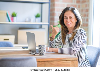 Middle age senior woman sitting at the table at home working using computer laptop pointing and showing with thumb up to the side with happy face smiling - Shutterstock ID 1527518858