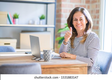 Middle age senior woman sitting at the table at home working using computer laptop happy with big smile doing ok sign, thumb up with fingers, excellent sign - Shutterstock ID 1531883147