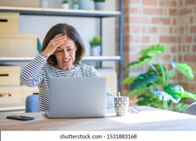 Middle Age Senior Woman Sitting At The Table At Home Working Using Computer Laptop Stressed With Hand On Head, Shocked With Shame And Surprise Face, Angry And Frustrated. Fear And Upset For Mistake.