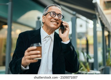 Middle Age Southeast Asian Man Speaking On The Phone And Drinking A Cup Of Coffee At The City