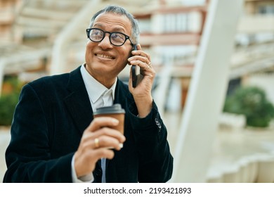 Middle Age Southeast Asian Man Speaking On The Phone And Drinking A Cup Of Coffee At The City