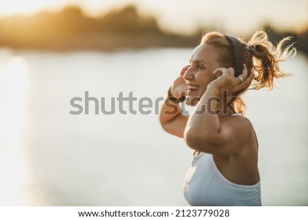 A middle age sportswoman listening to music and preparing to working out near to river, in the city.