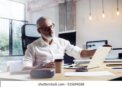 Middle age top manager wearing a classic glasses and working at the wood table in modern interior design office.Stylish bearded businessman using laptop on workplace. Horizontal,blurred - Powered by Shutterstock