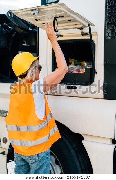 Middle age truck driver woman with vest and
helmet using storage for personal items, trucker occupation in
Europe for females