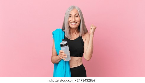 middle age white hair woman feeling shocked,laughing and celebrating success with a towel and water bottle. fitness concept - Powered by Shutterstock