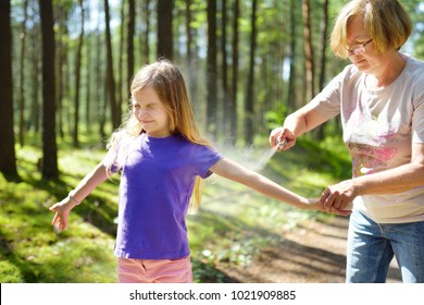 Middle Age Woman Applying Insect Repellent To Her Granddaughter Before Forest Hike Beautiful Summer Day. Protecting Children From Biting Insects At Summer. Active Leisure With Kids.