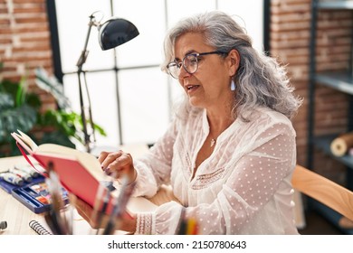 Middle age woman artist reading book at art studio - Powered by Shutterstock