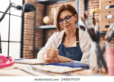 Middle age woman artist smiling confident drawing on notebook at art studio - Powered by Shutterstock