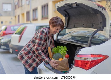 Middle Age Woman In Car Park, Loading Shopping Into Boot Of Car.