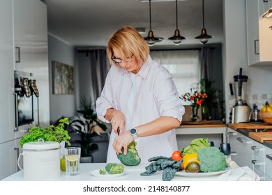 Middle Age Woman Cutting Broccoli While Cooking Healthy Dish For Lunch On The Kitchen. Healthy Lifestyle. Cooking At Home. Prepare Food. Vegetarian, Vegan Diet. Selective Focus