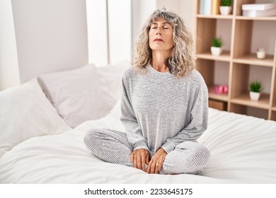 Middle age woman doing yoga exercise sitting on bed at bedroom - Powered by Shutterstock