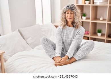 Middle age woman doing yoga exercise sitting on bed at bedroom - Powered by Shutterstock