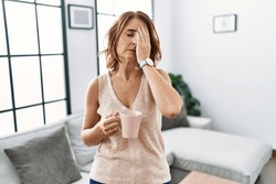 Middle Age Woman Drinking A Cup Coffee At Home Yawning Tired Covering Half Face, Eye And Mouth With Hand. Face Hurts In Pain. 