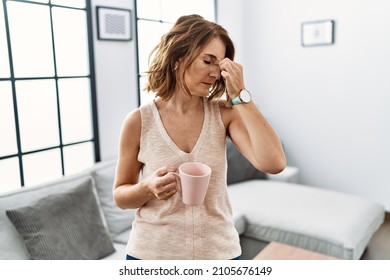 Middle Age Woman Drinking A Cup Coffee At Home Tired Rubbing Nose And Eyes Feeling Fatigue And Headache. Stress And Frustration Concept. 