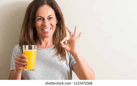 Middle age woman drinking orange juice in a glass doing ok sign with fingers, excellent symbol - Shutterstock ID 1115472368