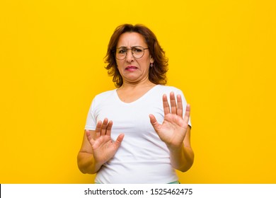 Middle Age Woman Feeling Disgusted And Nauseous, Backing Away From Something Nasty, Smelly Or Stinky, Saying Yuck Against Yellow Wall