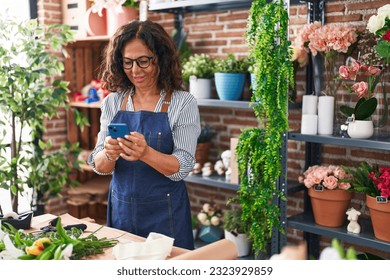 Middle age woman florist smiling confident using smartphone at flower shop - Powered by Shutterstock