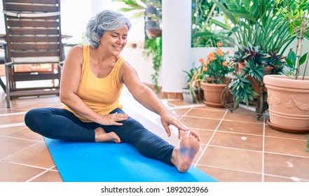 Middle age woman with grey hair smiling happy doing exercise and stretching on the terrace at home