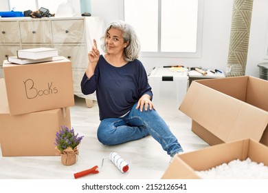 Middle Age Woman With Grey Hair Sitting On The Floor At New Home Pointing Finger Up With Successful Idea. Exited And Happy. Number One. 