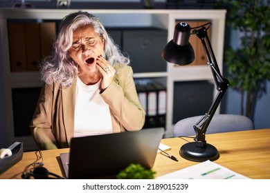 Middle Age Woman With Grey Hair Working Using Computer Laptop Late At Night Touching Mouth With Hand With Painful Expression Because Of Toothache Or Dental Illness On Teeth. Dentist 