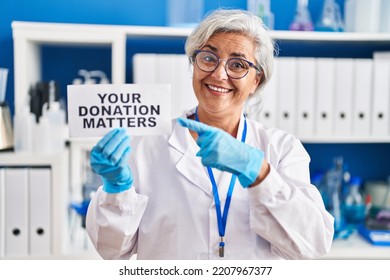 Middle Age Woman With Grey Hair Working At Scientist Laboratory Holding Your Donation Matters Banner Smiling Happy Pointing With Hand And Finger 