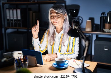 Middle Age Woman With Grey Hair Working At The Office At Night Showing And Pointing Up With Finger Number One While Smiling Confident And Happy. 