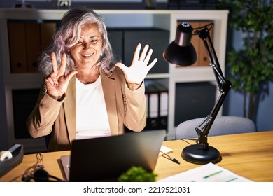 Middle Age Woman With Grey Hair Working Using Computer Laptop Late At Night Showing And Pointing Up With Fingers Number Eight While Smiling Confident And Happy. 