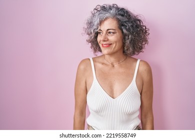 Middle age woman with grey hair standing over pink background looking away to side with smile on face, natural expression. laughing confident.  - Powered by Shutterstock