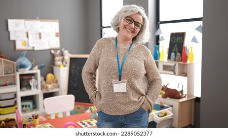 Middle age woman with grey hair preschool teacher smiling confident standing at kindergarten - Shutterstock ID 2289052377