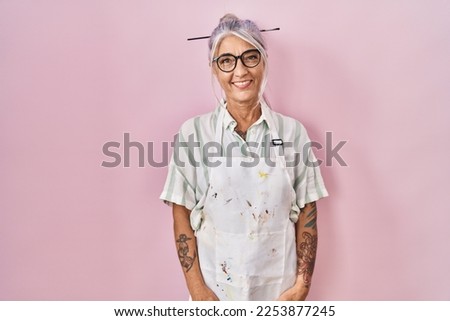 Middle age woman with grey hair wearing artist look looking positive and happy standing and smiling with a confident smile showing teeth 