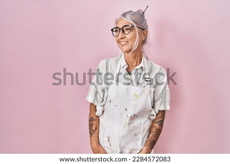 Middle age woman with grey hair wearing artist look looking away to side with smile on face, natural expression. laughing confident. 