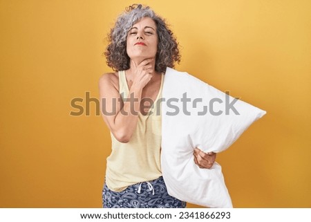 Middle age woman with grey hair wearing pijama hugging pillow touching painful neck, sore throat for flu, clod and infection 