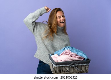 Middle age woman holding a clothes basket isolated on purple background celebrating a victory