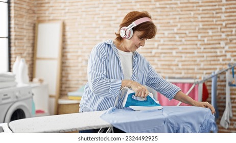 Middle age woman listening to music ironing clothes at laundry room - Powered by Shutterstock