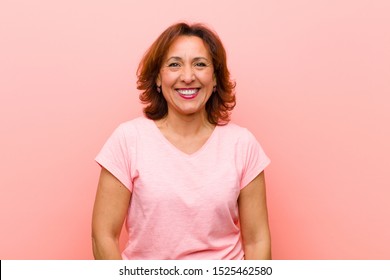 Middle Age Woman Looking Happy And Goofy With A Broad, Fun, Loony Smile And Eyes Wide Open Against Pink Wall