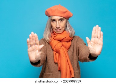 middle age woman looking serious, unhappy, angry and displeased forbidding entry or saying stop with both open palms - Shutterstock ID 2089999759