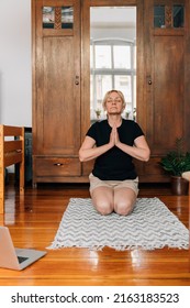 Middle Age Woman Mediating And Doing Yoga At Home With Laptop Online Class