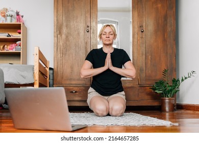 Middle Age Woman Mediating And Doing Yoga At Home With Laptop Online Class